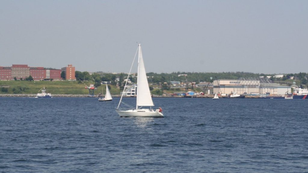 Sailboat on Halifax Harbour with the Dartmouth waterfront and industrial port in the background, Nova Scotia.